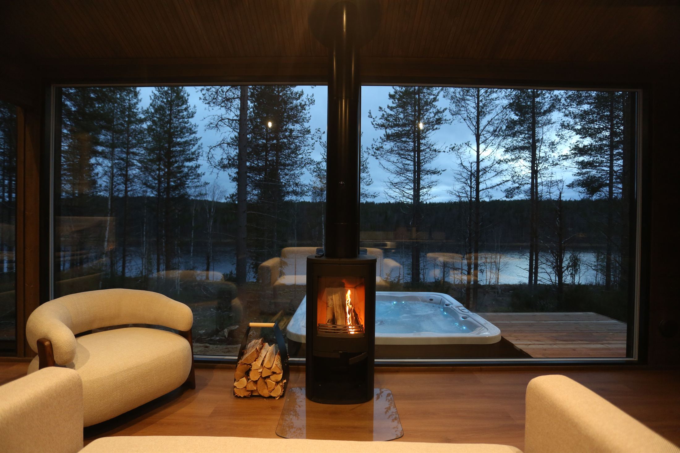 Living room with a wood stove, the hot tub outside and the Ounasjoki beyond the glass wall